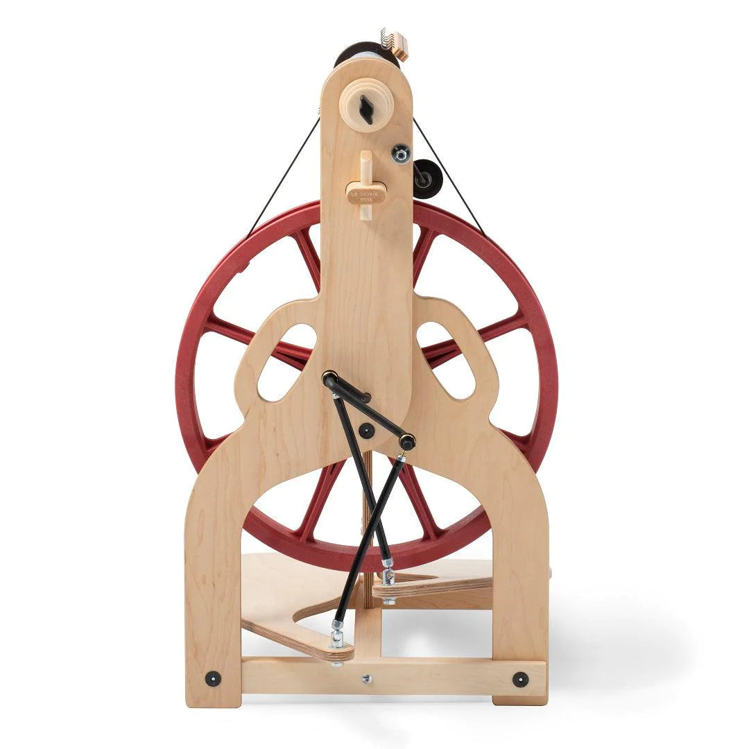 A rear perspective of the Ladybug Spinning Wheel illustrates the wheel's Scotch tension, double drive, and bobbin lead features. The image highlights the wheel's functional yet stylish construction, complete with accessories like the travel bobbins and whorls that support a range of yarn spinning techniques for the fiber enthusiast