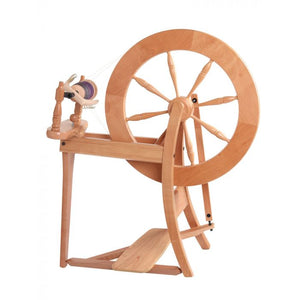 An artisan-crafted double drive spinning wheel with a rich natural wood texture, presenting a large, intricately designed wheel and sturdy foot pedal. Ideal for fiber artists, it combines traditional style with functionality for an exceptional spinning experience.