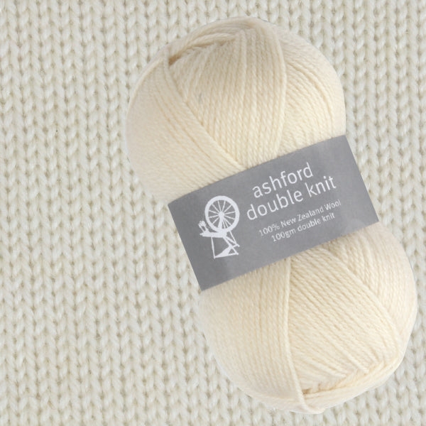 Ball of cream yarn with 'ashford double knit' label on a beige knitted wool fabric background